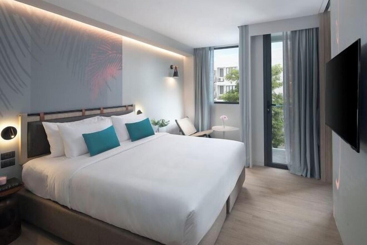 A modern hotel room with a large bed, bedside tables, a TV, and a window with curtains.