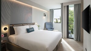 A modern hotel room with a large bed, a flat-screen TV, a chair, and a balcony with a view of the city. - JonoX Phuket Karon Hotel (Karon)