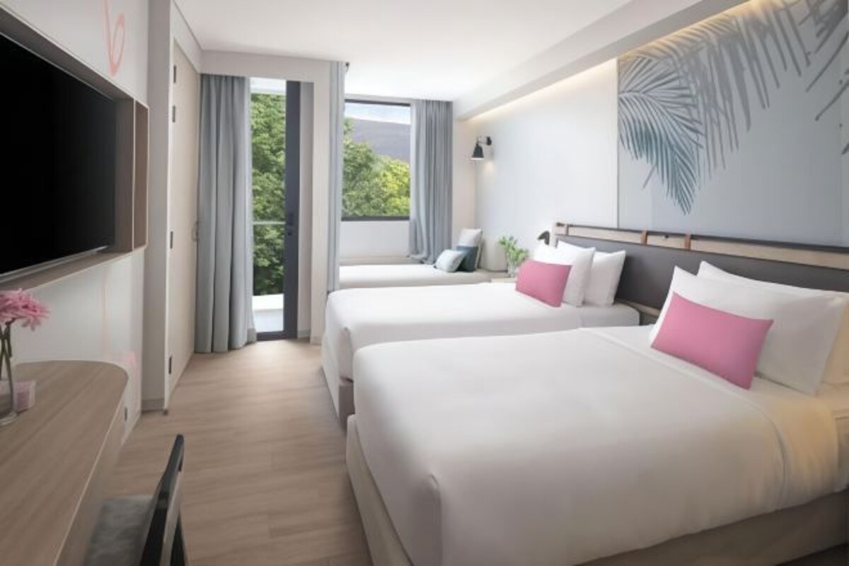 A hotel room with two beds, a flat-screen TV, a dining table, and a large window with a view of greenery.