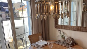 Un comedor con una mesa redonda de madera, sillas de mimbre con cojines oscuros y una lámpara colgante con cubiertos.