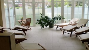 Una habitación soleada con varios sillones y una mesa, una planta en maceta y ventanas grandes que dan a vistas del exterior.