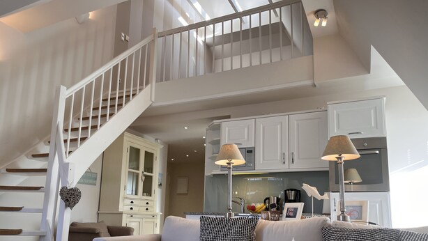 Un espacio habitable amplio con una escalera, una cocina al fondo y una zona de estar acogedora.