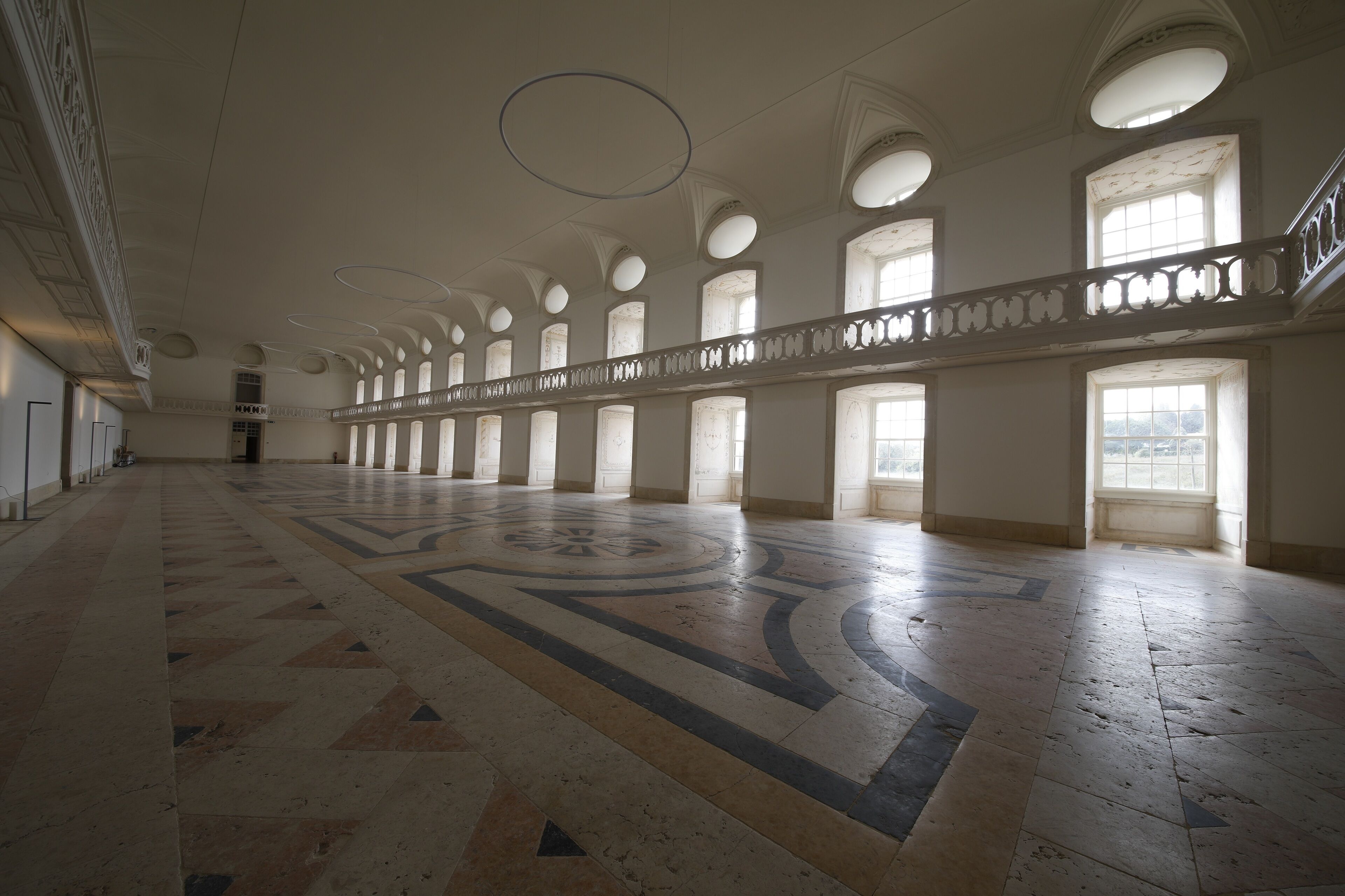 A spacious hall with a patterned floor, large windows, and a balcony with ornate railings.