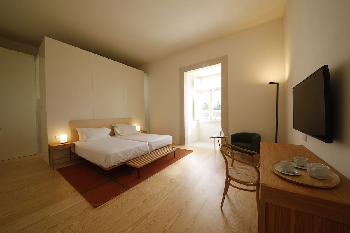 Une chambre à coucher avec un lit, des tables de chevet, un bureau avec des tasses, une chaise et un téléviseur fixé au mur.