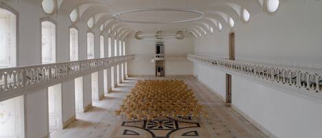 A long corridor with ornate white railings, a patterned floor, and a series of circular windows.