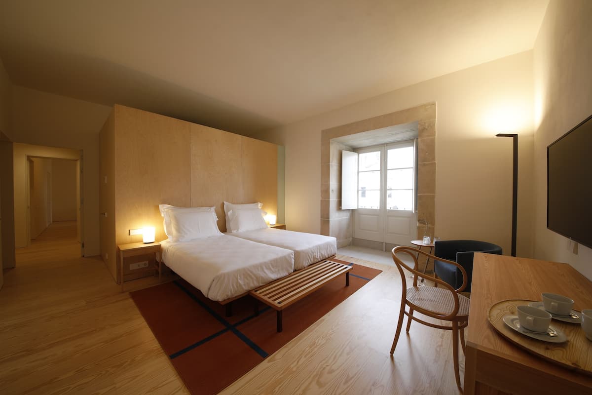 Une chambre d’hôtel moderne avec deux lits, un banc en bois, une table à manger avec des chaises et un téléviseur.