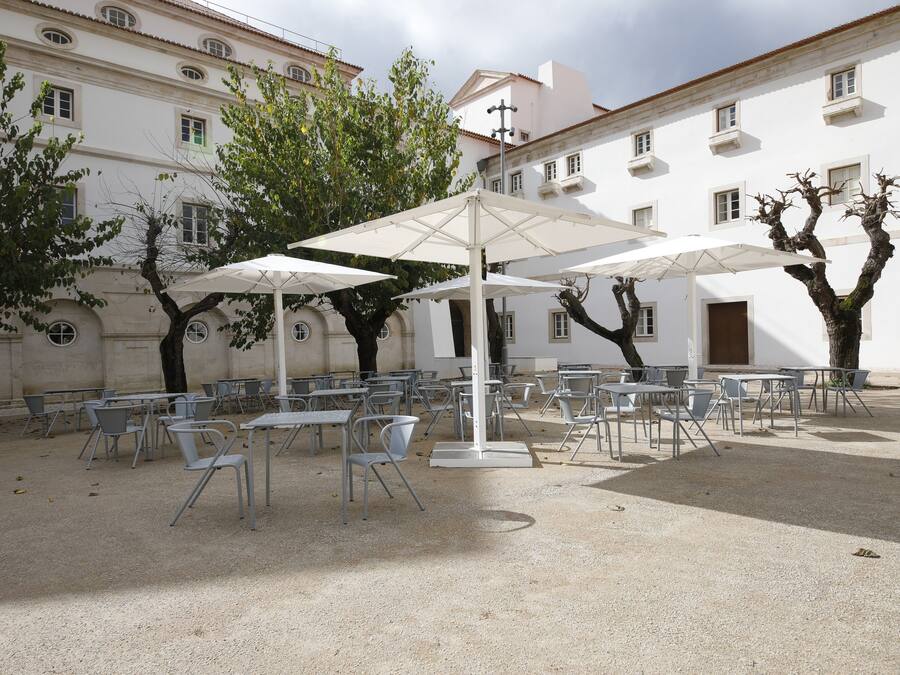 An outdoor seating area with tables and chairs, surrounded by trees and a white building with multiple windows.