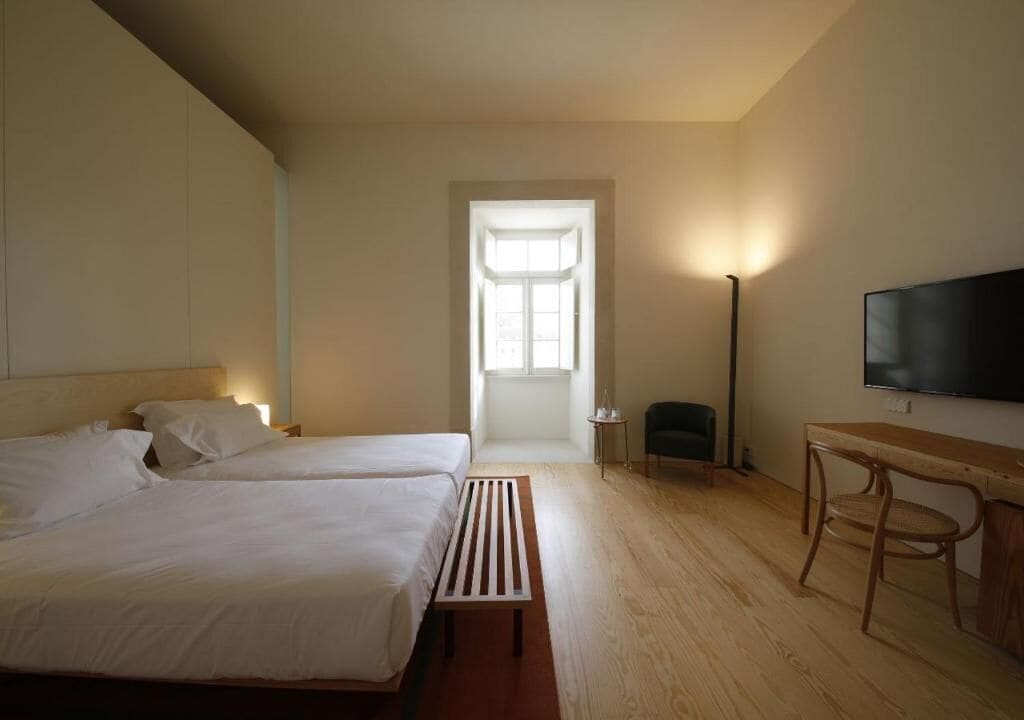 Habitación de hotel con dos camas, un escritorio, una silla, un televisor y una ventana.