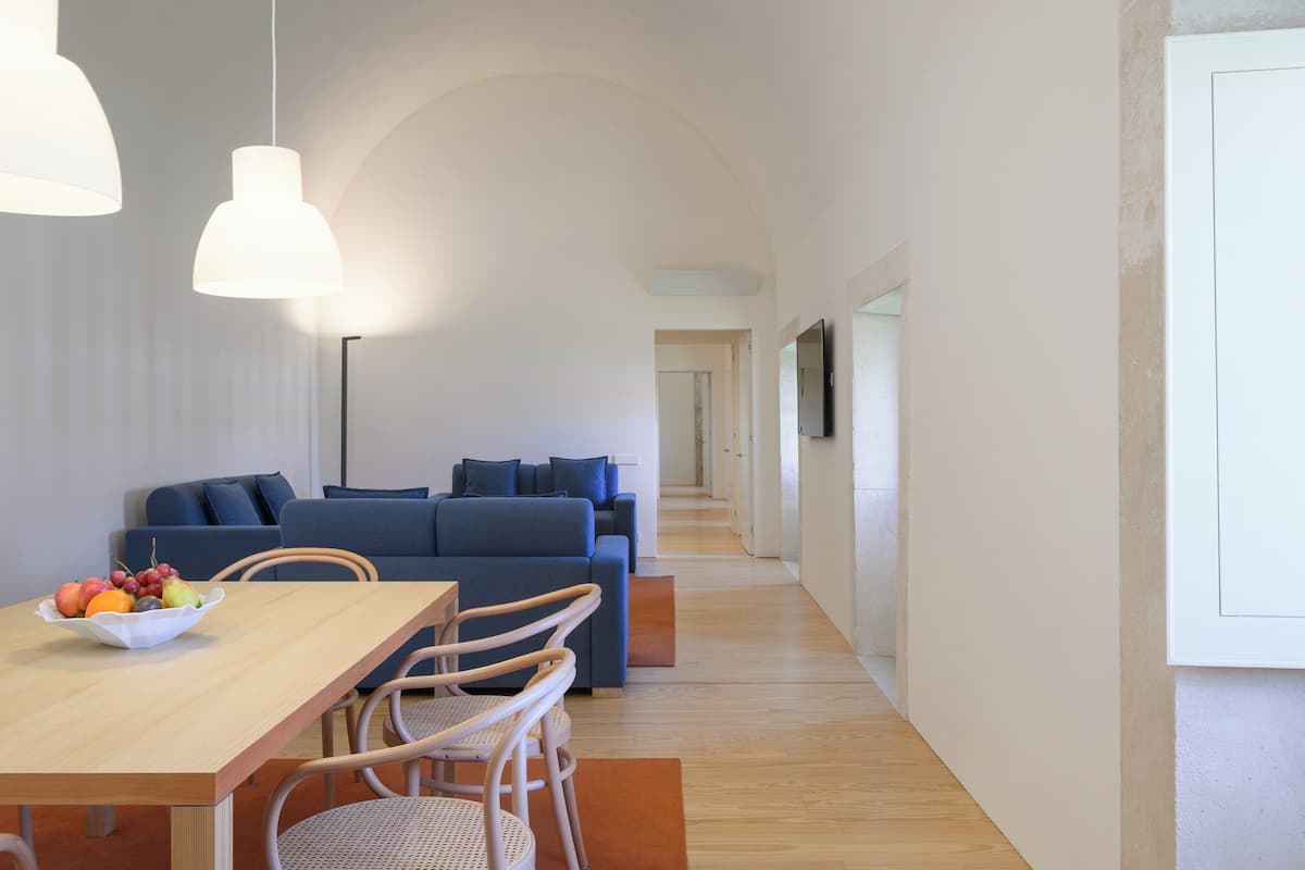 Un salon moderne avec un canapé, une table à manger et des chaises. On peut voir un panier de fruits sur la table.