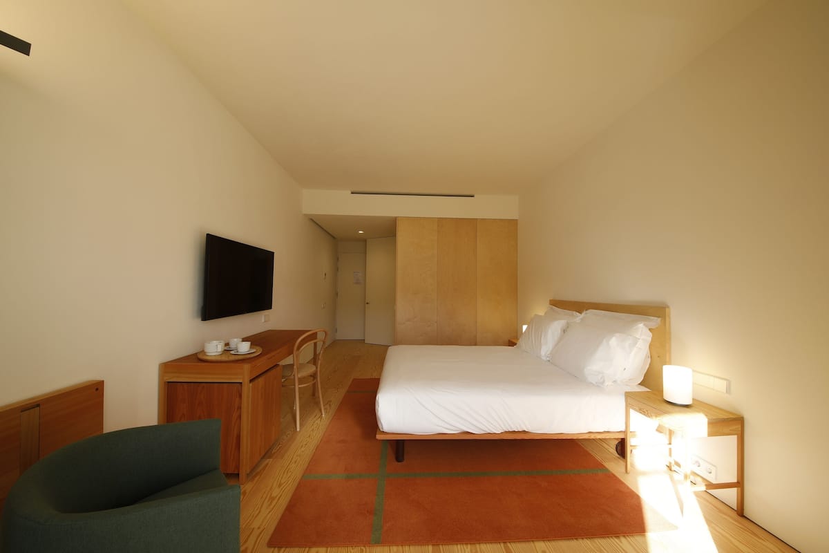 Une chambre d’hôtel comprenant un lit, un bureau avec une chaise, une télévision et une table de chevet avec une lampe.