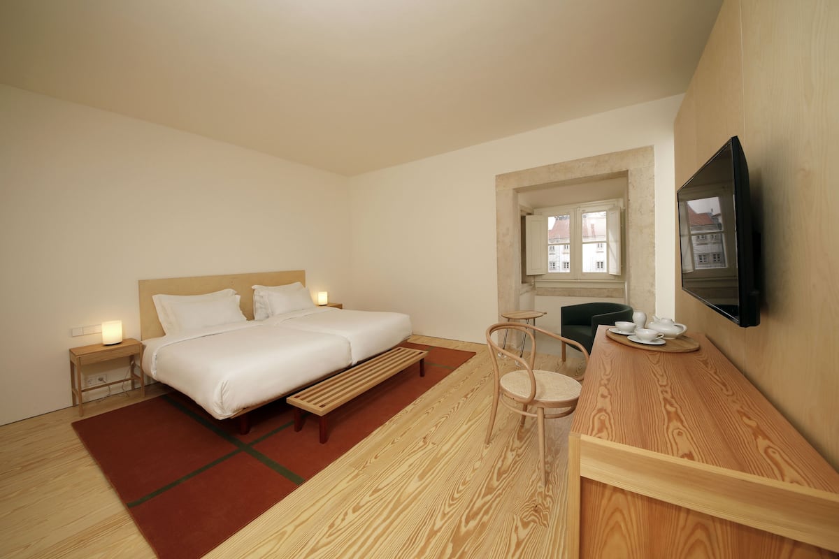 Une chambre d’hôtel moderne avec un grand lit, un banc en bois, une petite table avec des tasses et un téléviseur fixé au mur.