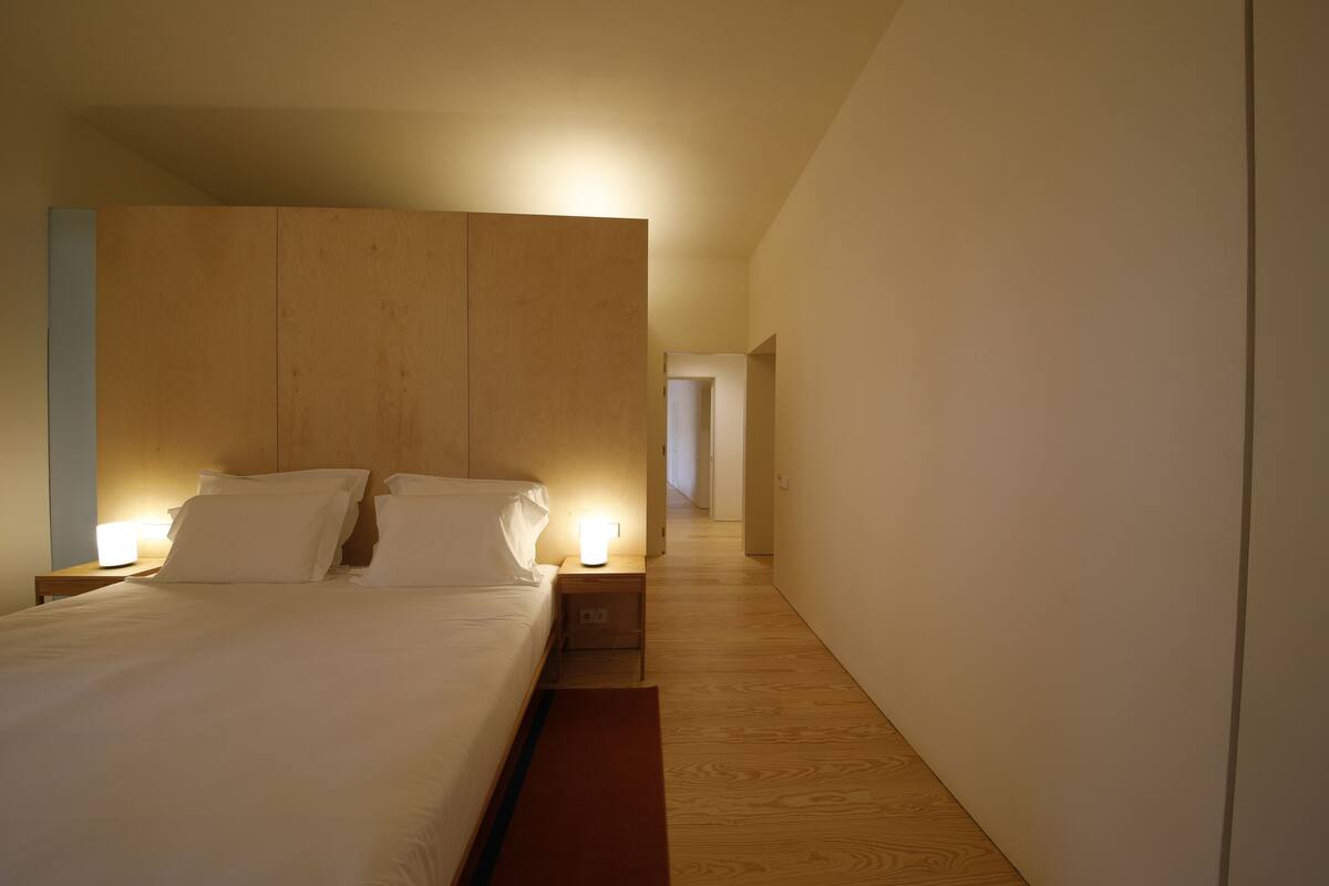Une chambre d’hôtel moderne avec un grand lit, des lampes de chevet et une tête de lit en bois.