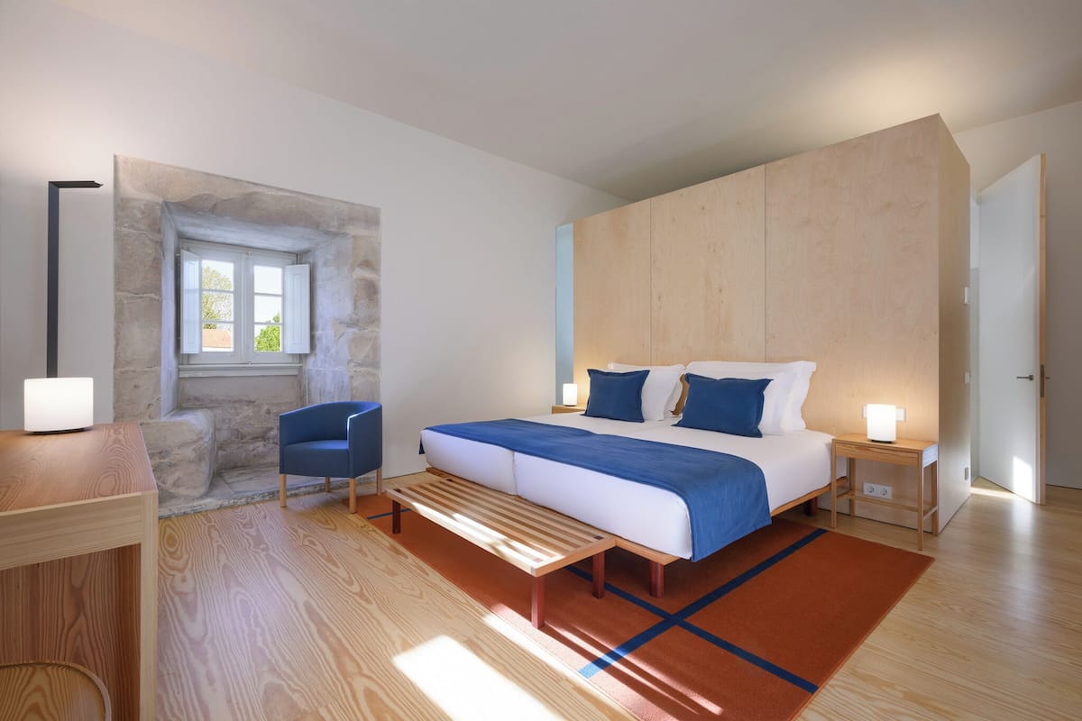 Une chambre moderne avec un grand lit, un banc, une chaise et un mur en pierre.
