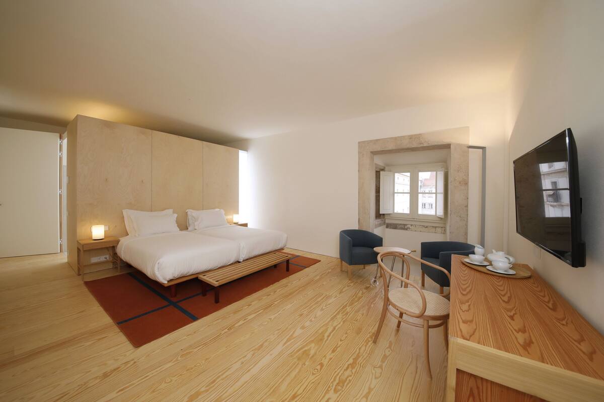Une chambre à coucher avec un lit, des tables de chevet, un bureau, des chaises, une télévision et une fenêtre.