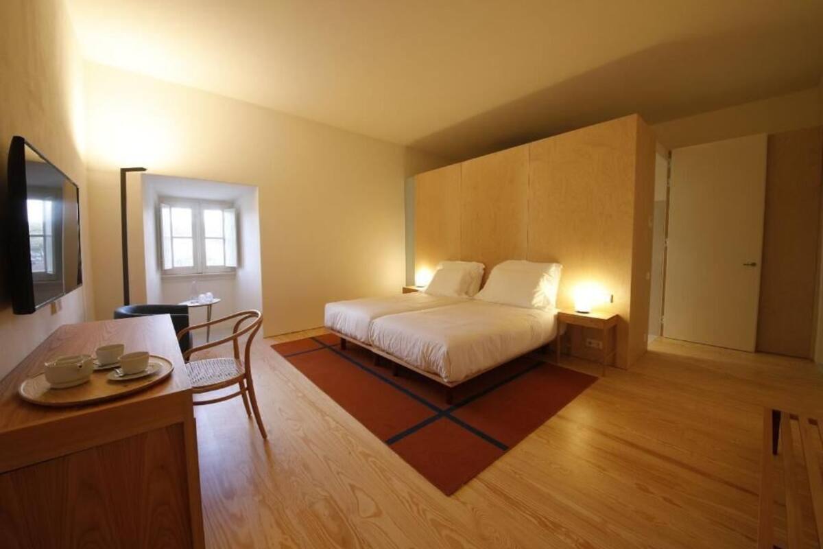 Une chambre à coucher avec un lit, des tables de chevet, un bureau avec des tasses, une chaise, une télévision et une fenêtre.