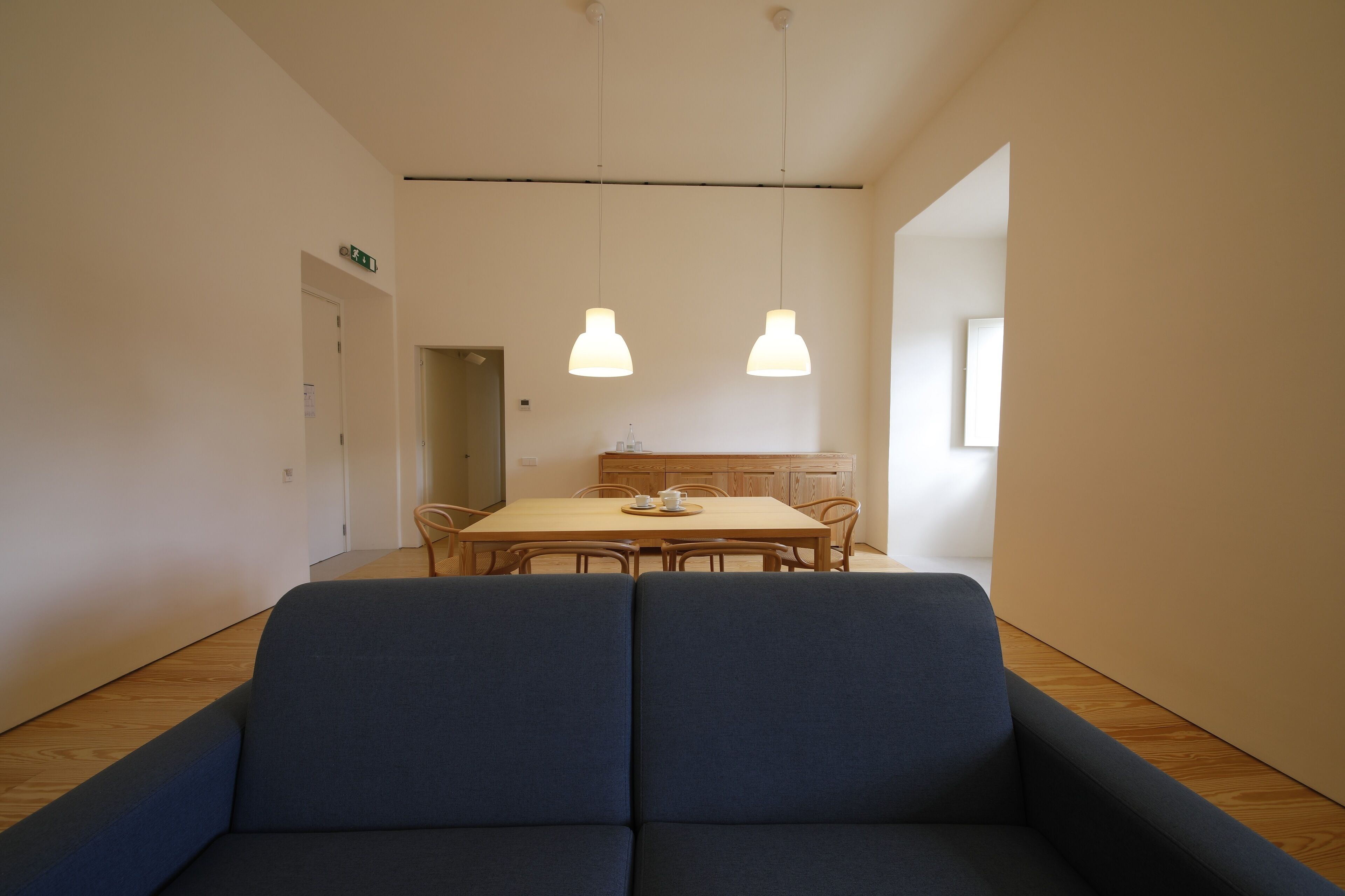 Un interior moderno con un comedor que incluye una mesa y sillas de madera, un sofá azul e iluminación colgante.