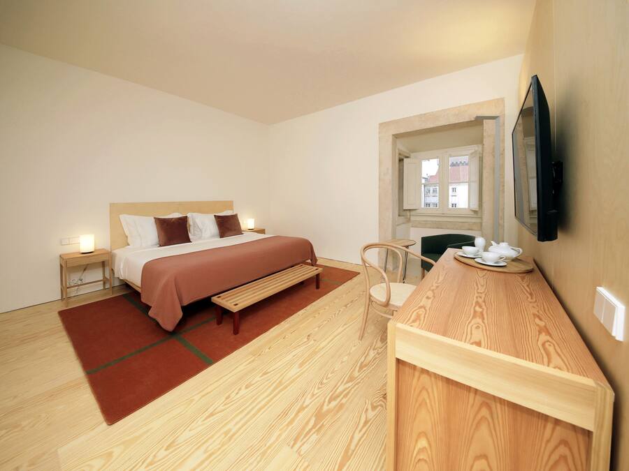 Una habitación de hotel moderna con cama, mesita de noche, silla y un escritorio de madera con espejo.