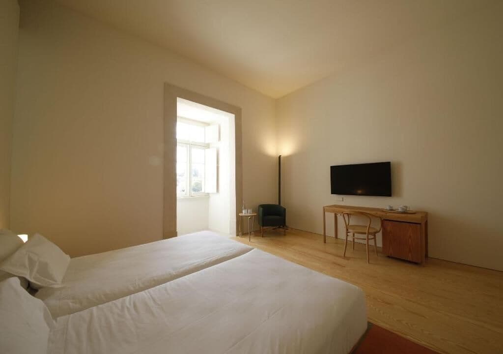 A hotel room with two beds, a desk, a chair, a TV, and a window.