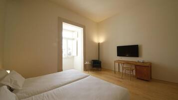 A hotel room with two beds, a desk, a chair, a TV, and a window.