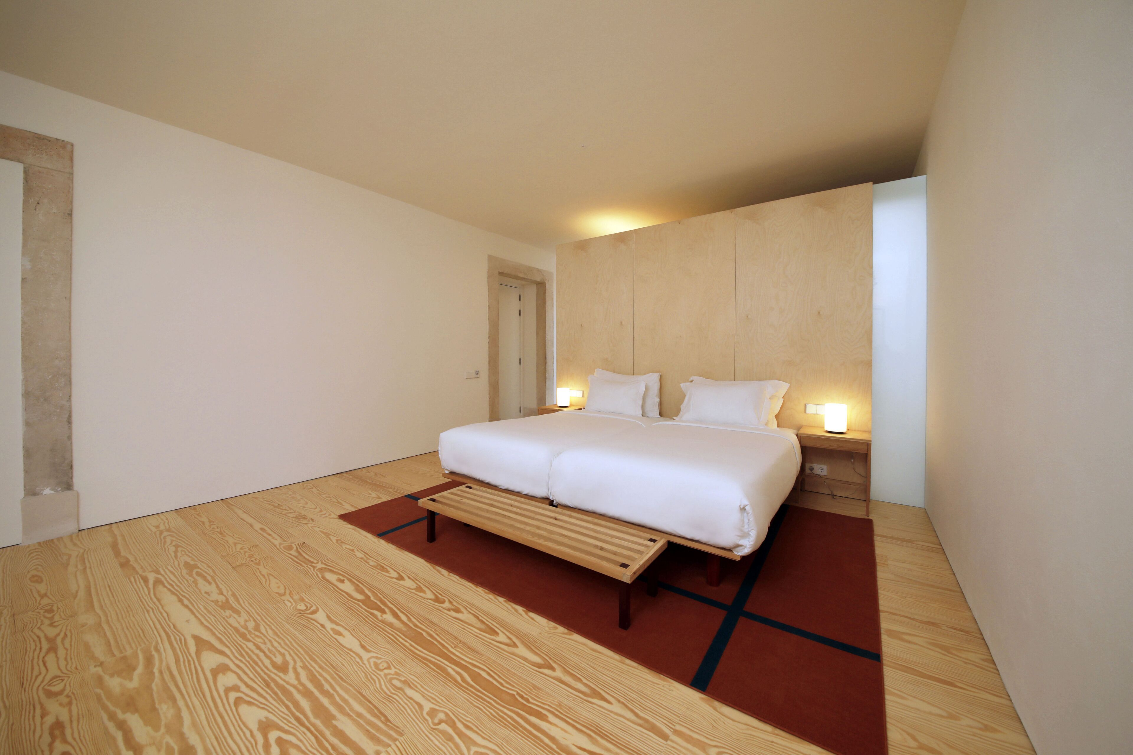 Ein modernes Schlafzimmer mit Holzboden, einem Bett mit weißer Bettwäsche und einem Nachttisch mit Lampe.