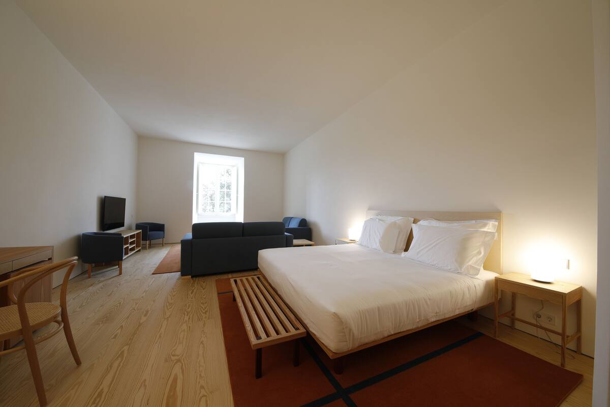 Une chambre d’hôtel moderne dotée d’un grand lit, d’un bureau, d’un canapé, d’une télévision et d’une fenêtre laissant entrer la lumière naturelle.