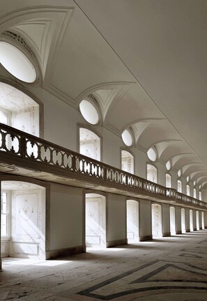 A grand corridor with high ceilings, arched windows, and a patterned floor. - Montebelo Mosteiro de Alcobaça Historic Hotel (Alcobaça)