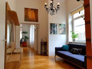 Een ruime woonkamer met een houten vloer, een blauwe bank, een kroonluchter en kunstwerken aan de muren.