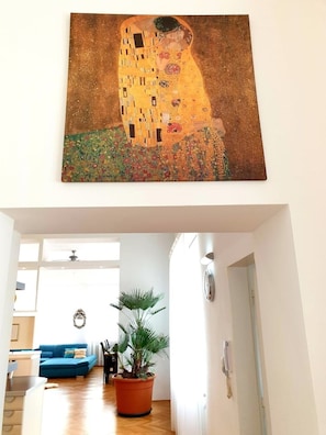 Een woonkamer met een groot schilderij van een omhelzend stel, een blauwe bank en een potplant.