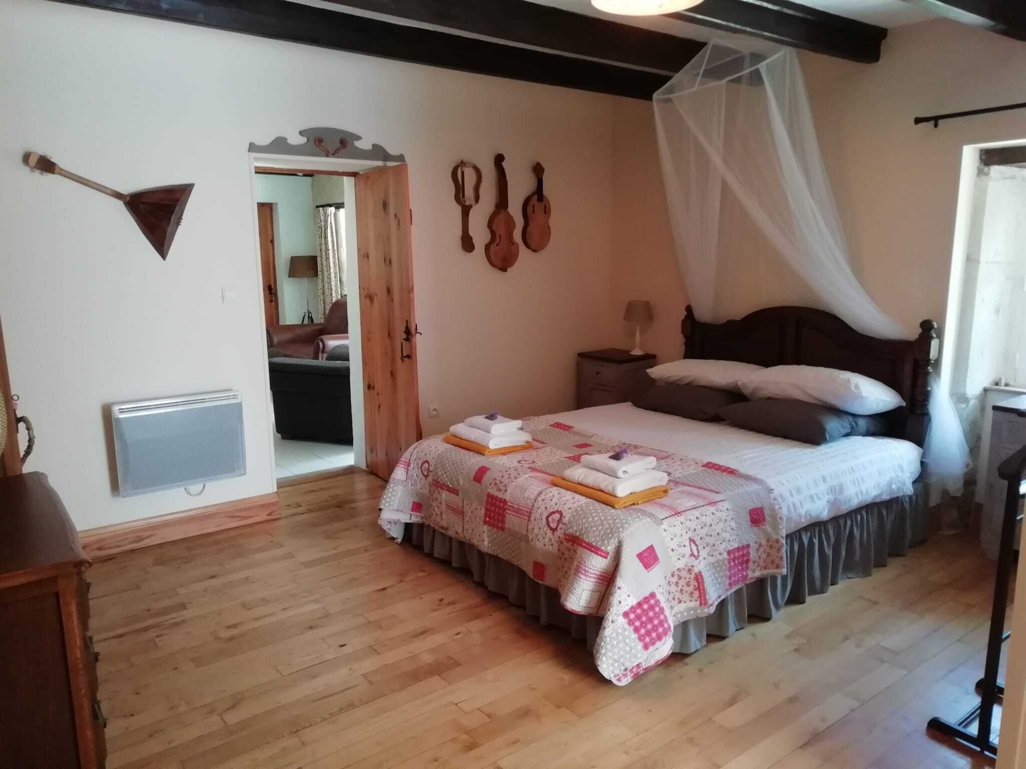 A bedroom with a bed, a bedside table, a nightstand, a wooden floor, a radiator, and a window with a curtain.