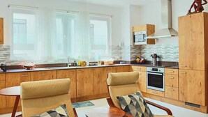 Een moderne keuken met houten kasten, een ingebouwde oven en een magnetron. Er staan twee stoelen met kussens bij een kleine tafel.