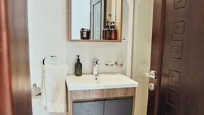 Een badkamer met een witte wasbak, een spiegel en een houten kastje eronder.