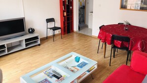 Ein Wohnzimmer mit Flachbildfernseher, Bücherregal, Esstisch mit Stühlen und einem roten Sofa.