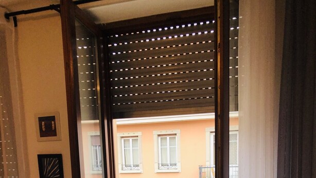 Ein Zimmer mit einer Schiebeglastür, die auf einen Balkon mit Metallgeländer und einem Stuhl führt.