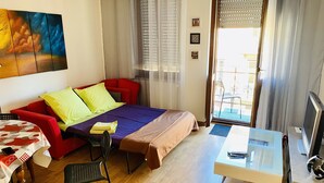 Ein Hotelzimmer mit einem Bett, einer roten Couch, einem kleinen Tisch mit Stuhl, einem Fernseher und einem Gemälde an der Wand.