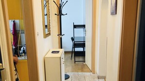 Ein Flur mit Fliesenboden, einem Kleiderständer, einer kleinen Kommode und einem Stuhl.