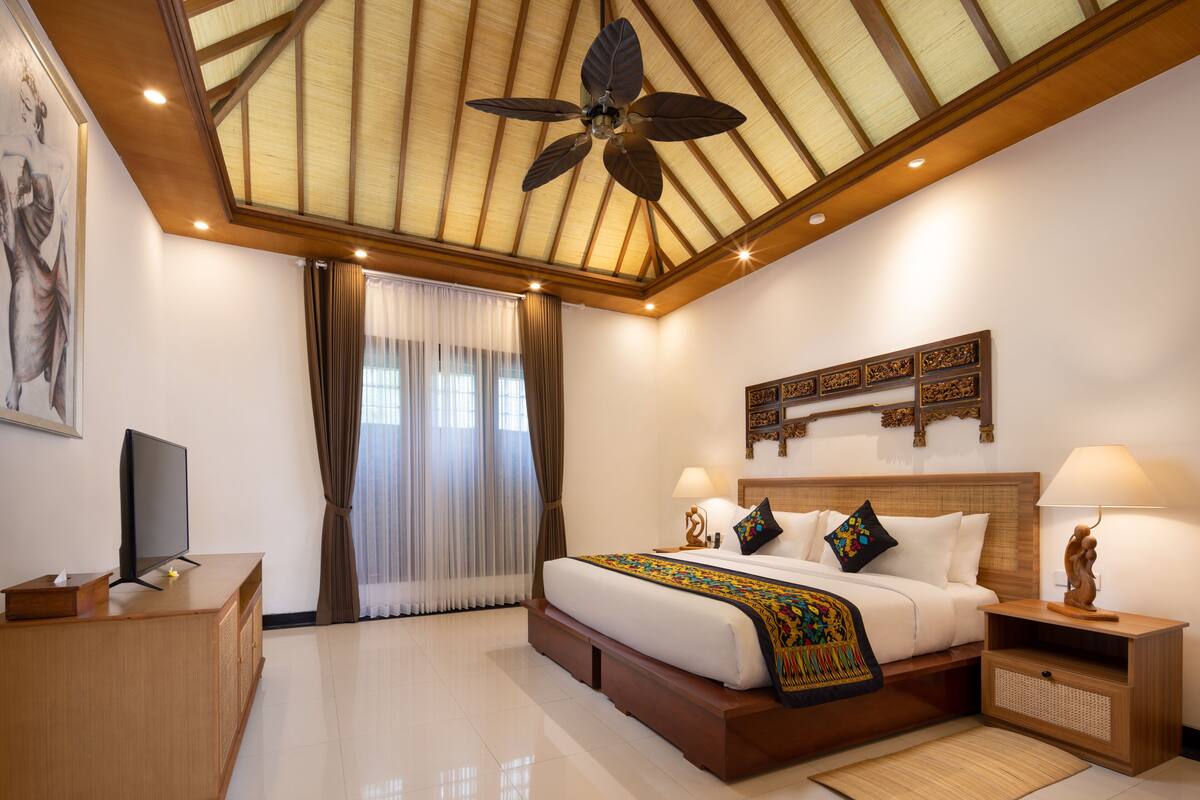 A hotel room with a large bed, a ceiling fan, a TV, and a wooden headboard.