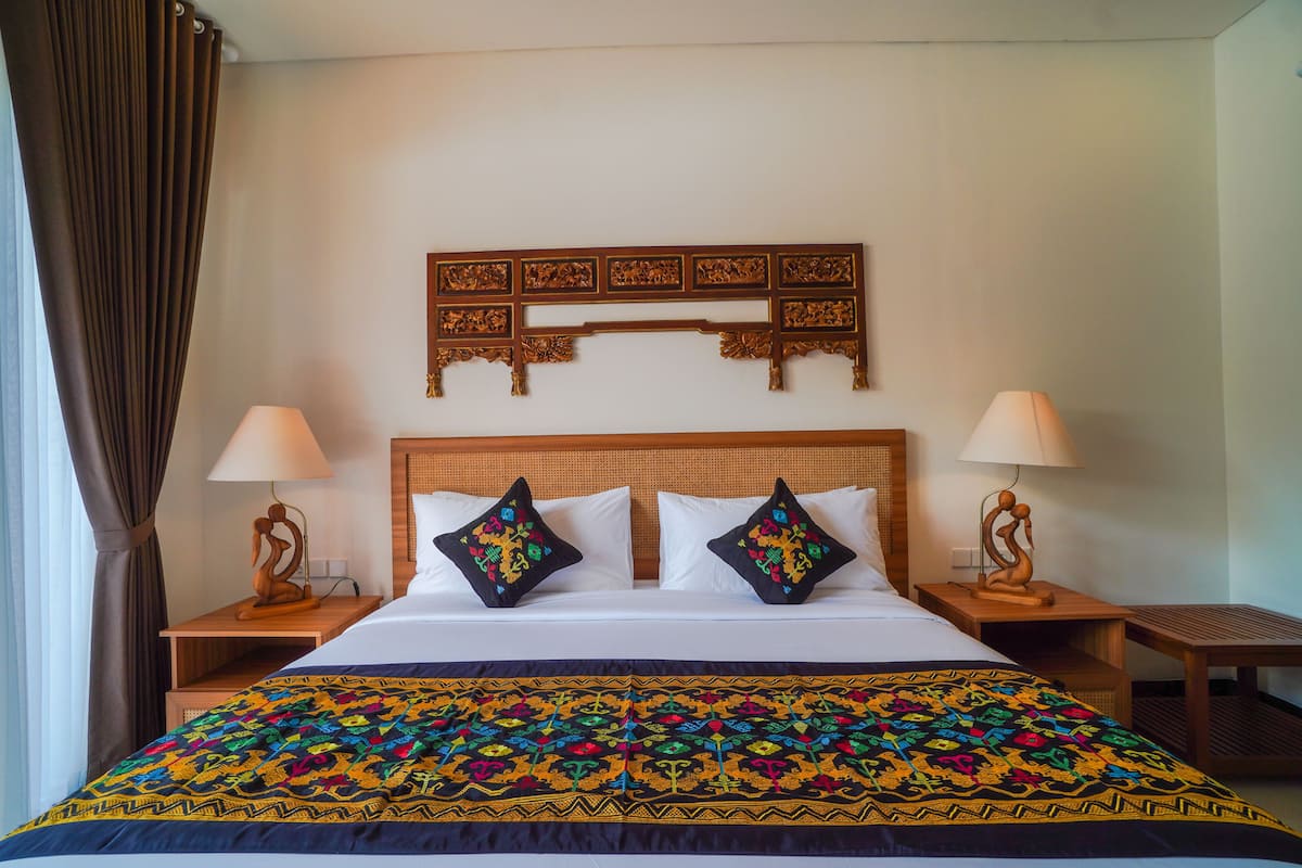 A hotel room with a large bed, two bedside tables with lamps, a decorative headboard, and a colorful bedspread.