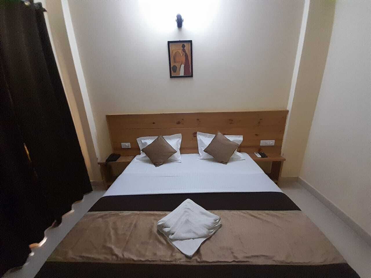 A bedroom with a wooden headboard, a bed with white linens and two pillows, a bedside table, and a wall-mounted light fixture.