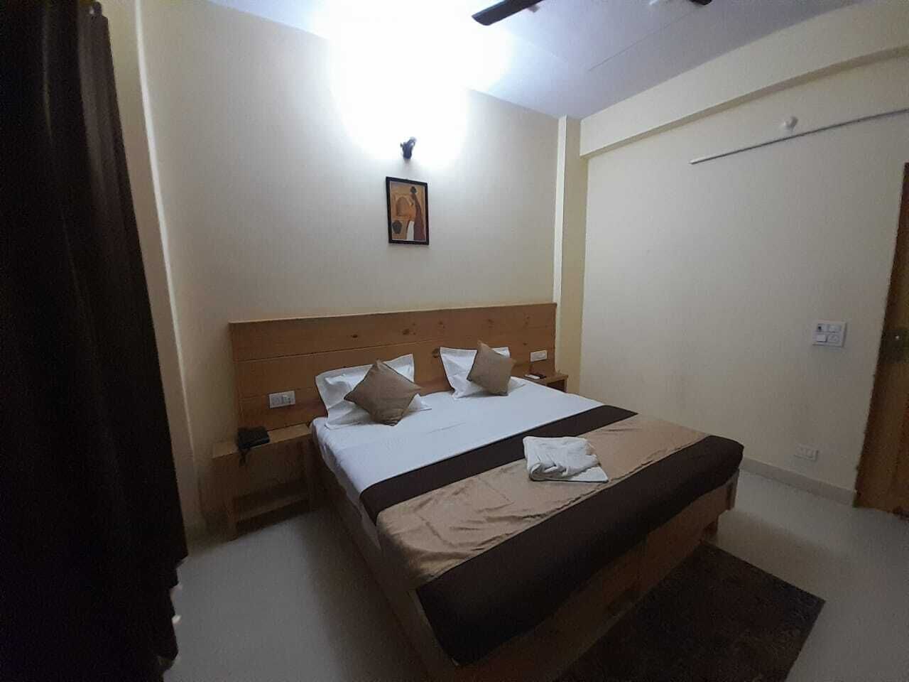 A hotel room with a bed, a nightstand, a wall-mounted light, and a door.