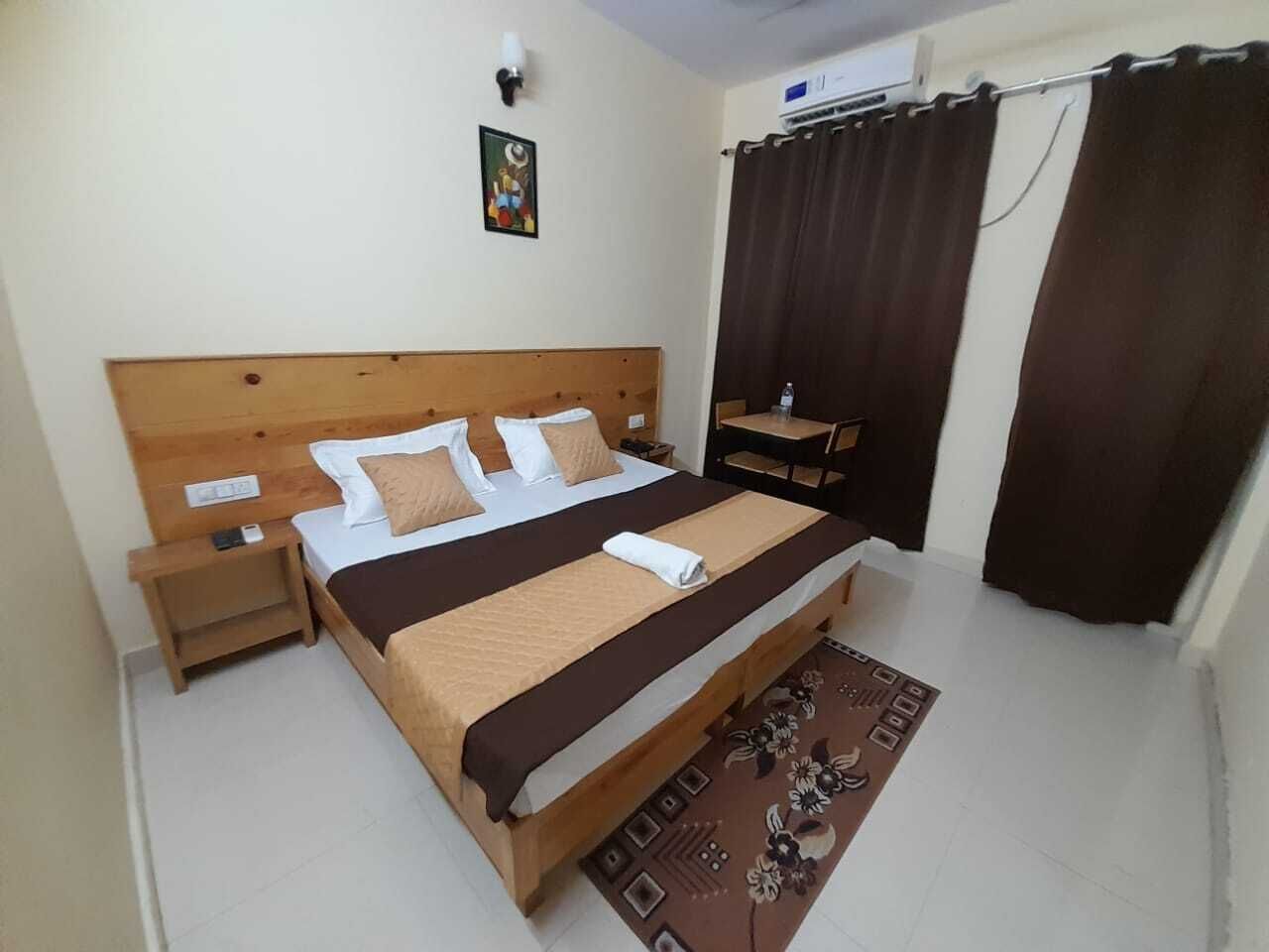 Une chambre avec un lit en bois, une table de chevet, un climatiseur fixé au mur et un rideau.