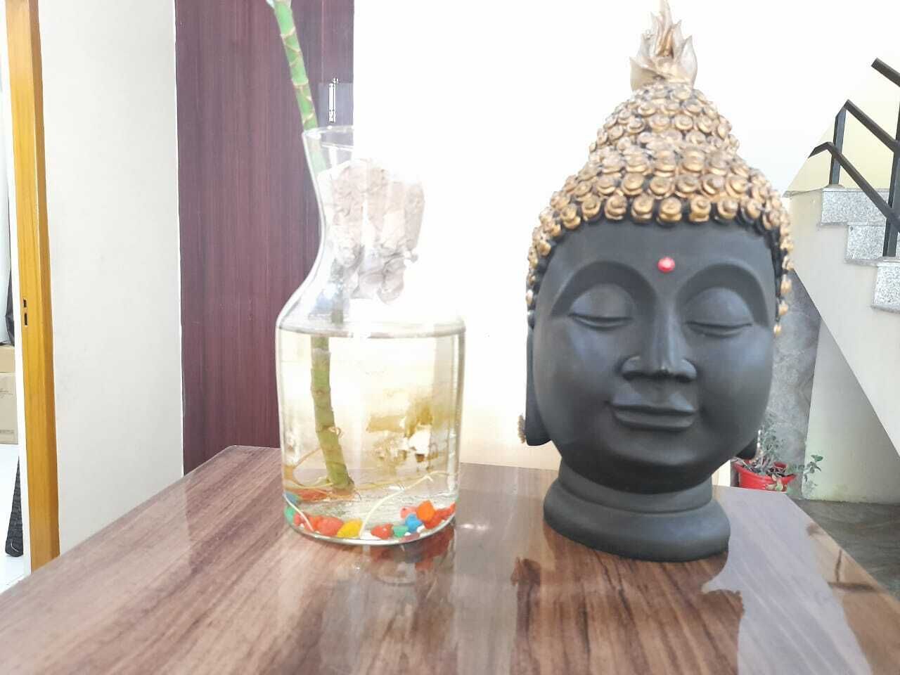 A wooden table with a glass vase containing a plant and colorful pebbles, and a Buddha statue.