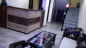 A reception area with a wooden reception desk, a glass-top coffee table, and a staircase with red and white balloons. - Hotel Krishna Rishikesh (Narendranagar)