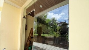 A glass door leading to a paved area with potted plants and a ladder. - Hotel Krishna Rishikesh (Narendranagar)