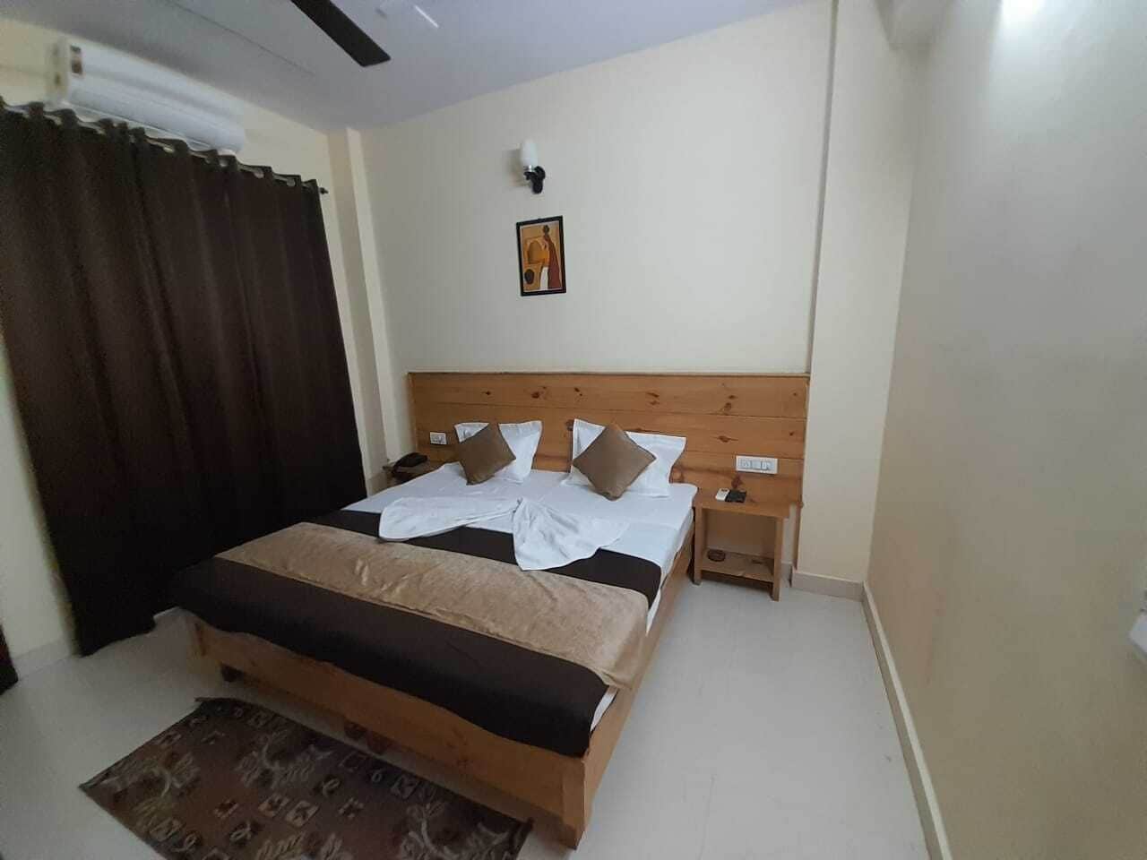 A bedroom with a wooden bed, a nightstand, a wall-mounted lamp, and a framed picture.