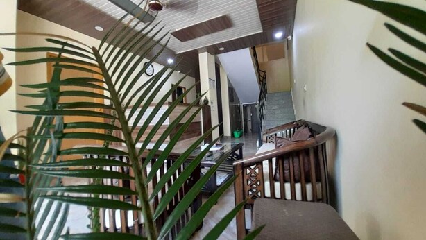 A staircase with a wooden railing, a ceiling fan, and a plant in the foreground. - Hotel Krishna Rishikesh (Narendranagar)