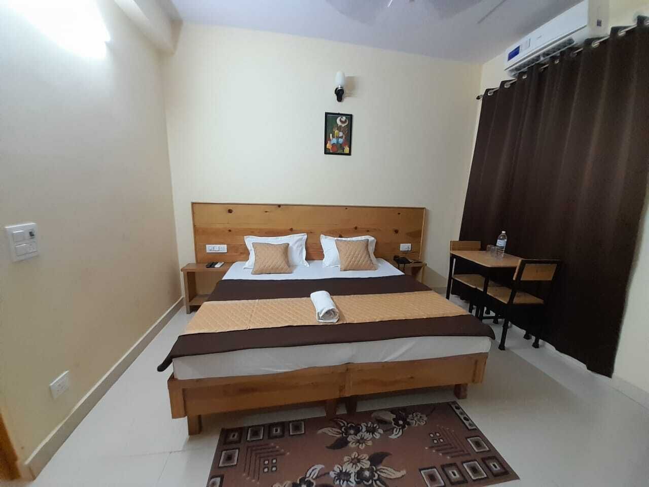 Habitación de hotel con cama doble, un pequeño escritorio, una silla, una mesita de noche y una lámpara de pared.
