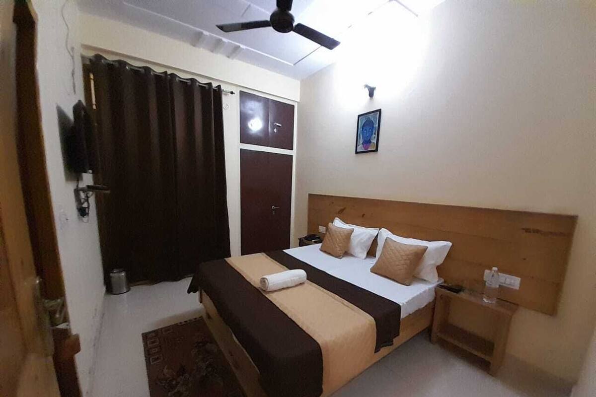 A bedroom with a bed, a nightstand, a ceiling fan, a window with curtains, and a door.