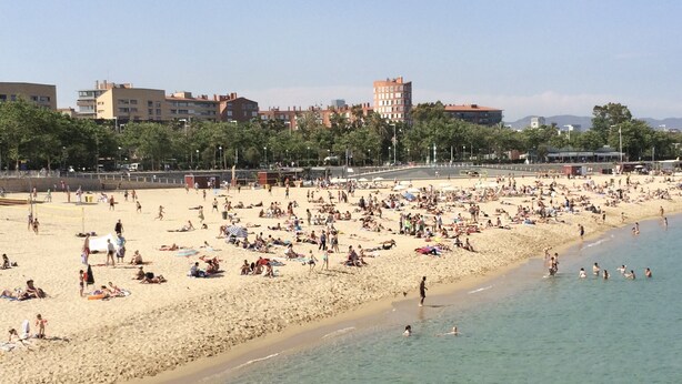 Une plage bondée où les gens se prélassent au soleil et se baignent.