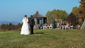 A wedding ceremony outdoors with a gazebo and guests seated on white chairs. - 100+ Acre Farm Retreat for Groups, Yoga, Weddings (Greensboro Bend)