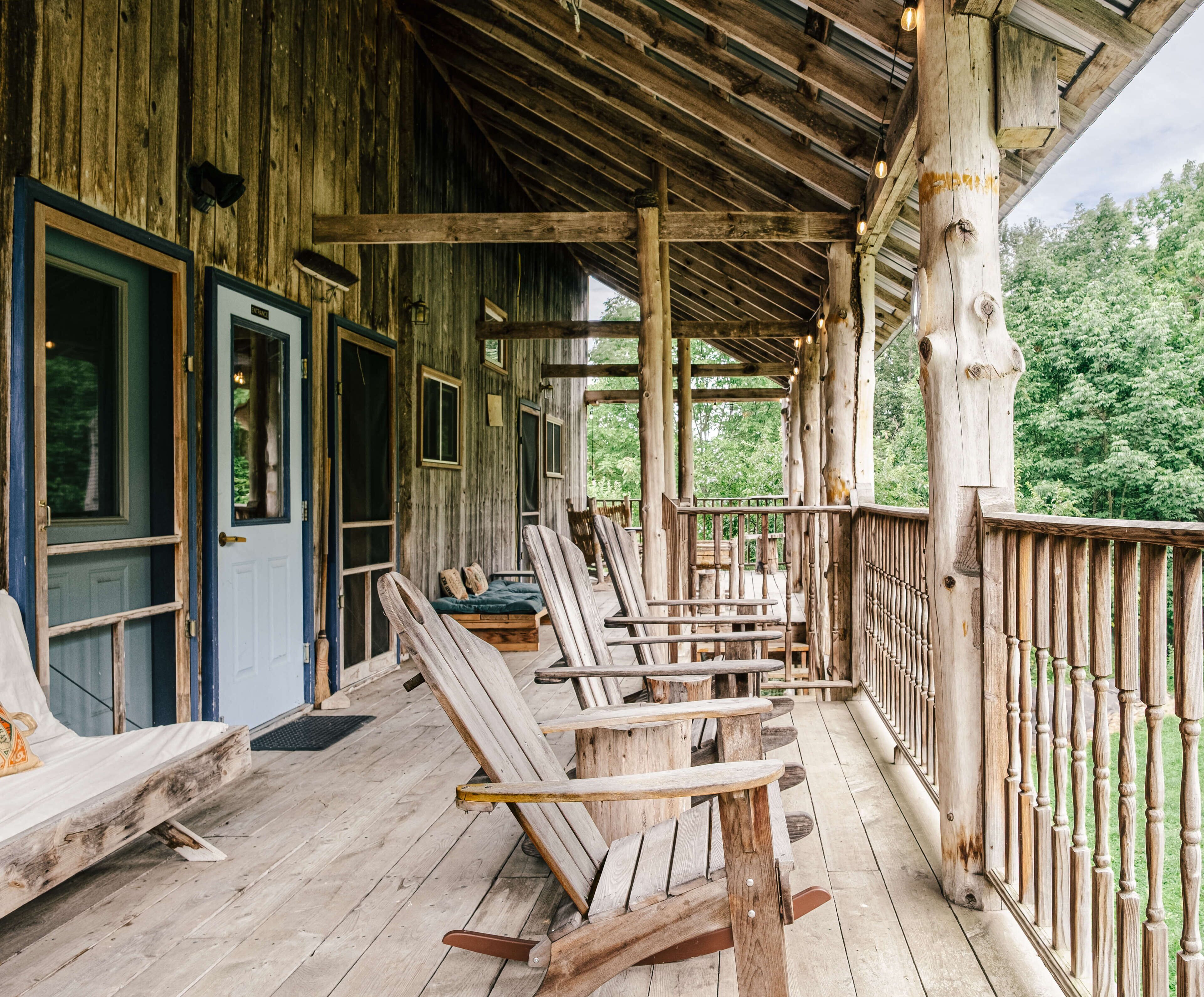 Une véranda rustique en bois, dotée de plusieurs fauteuils à bascule et d’une clôture en bois.